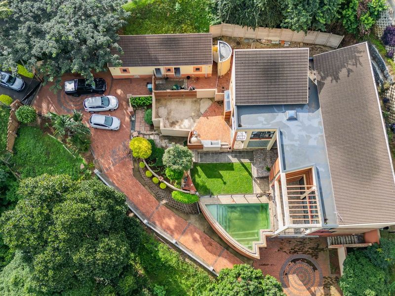 Aerial view of the property featuring a paved driveway, landscaped garden, swimming pool, and multi-level roof structure.