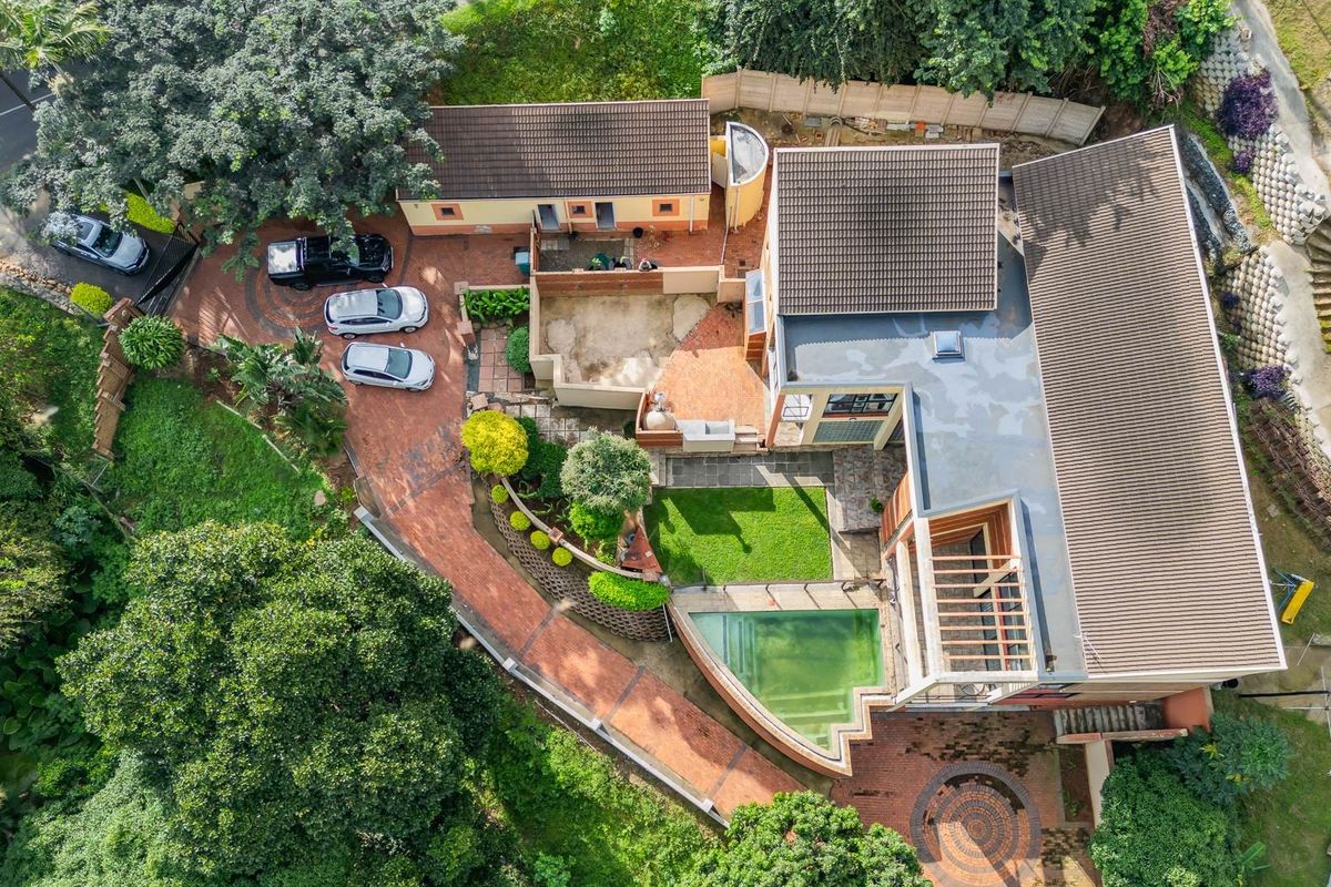 Aerial view of the property featuring a paved driveway, landscaped garden, swimming pool, and multi-level roof structure.