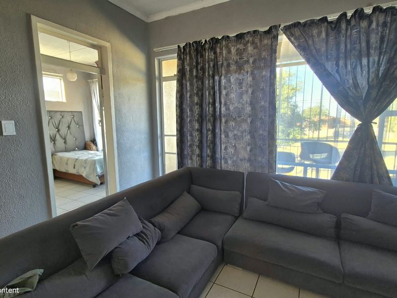 A living room area featuring tiled flooring and a sliding door with security gate, providing access to an outdoor space.