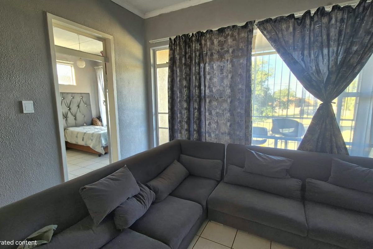 A living room area featuring tiled flooring and a sliding door with security gate, providing access to an outdoor space.