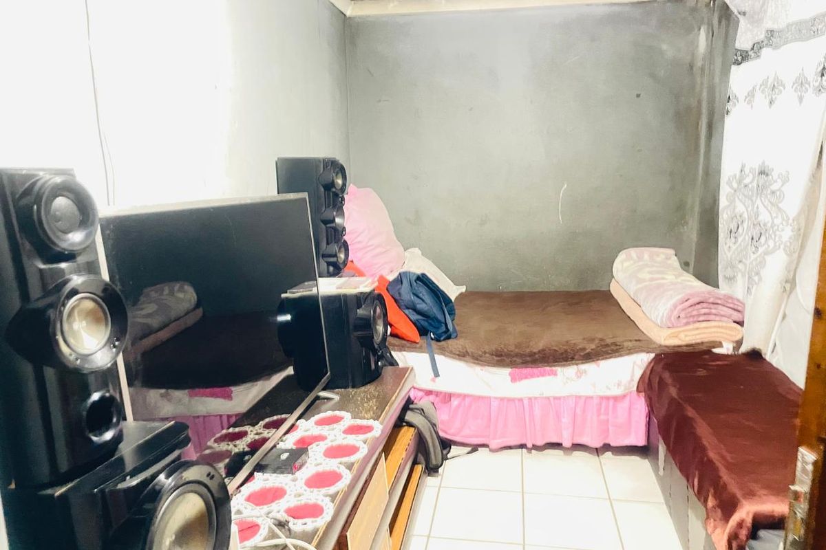 A compact bedroom featuring tiled flooring and unfinished grey plaster walls, offering a basic living space.