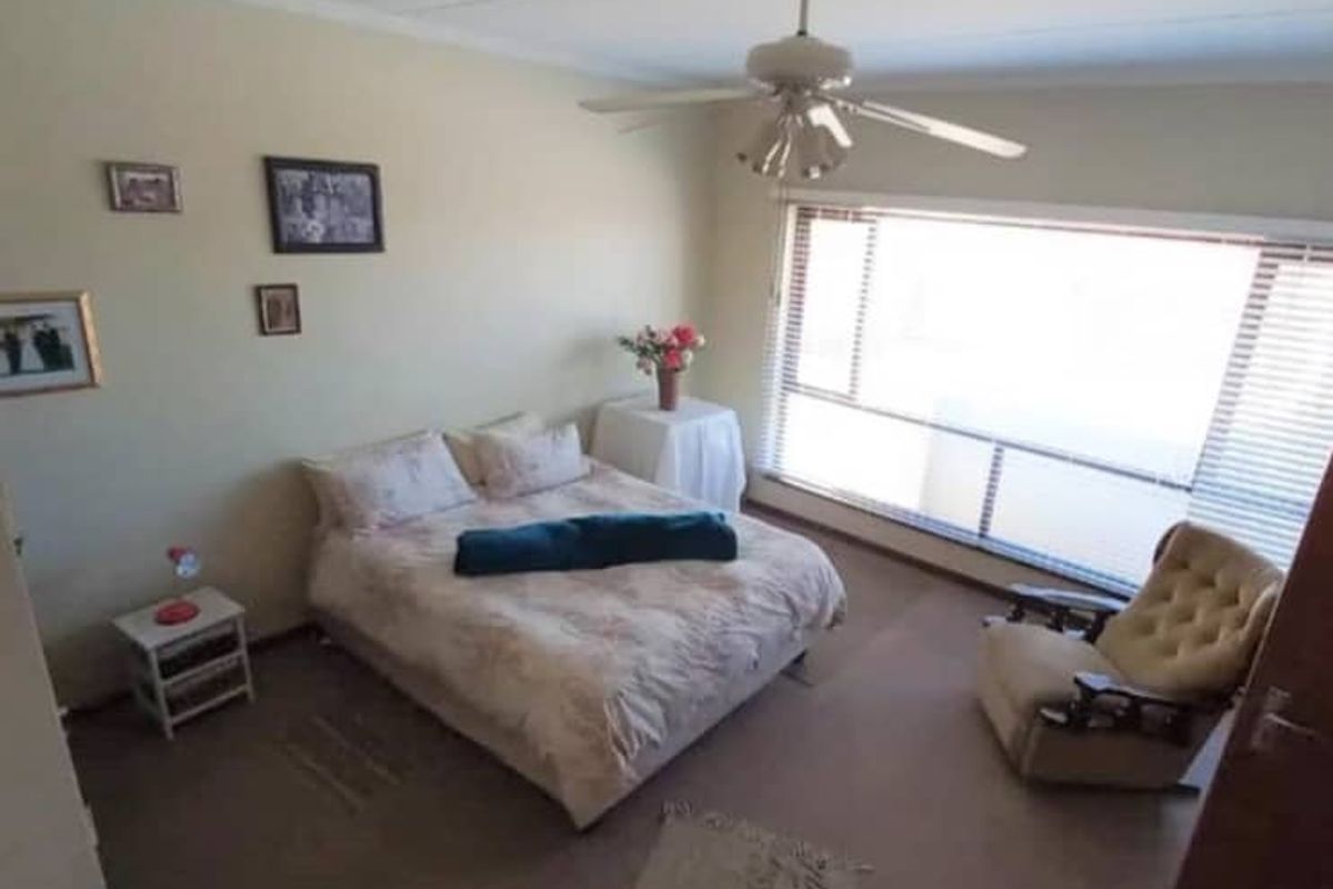 A spacious bedroom featuring a large window with horizontal blinds, a ceiling fan, and neutral wall finishes.