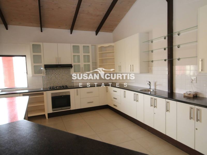 Spacious kitchen featuring white cabinetry, dark countertops, gas hob, built-in oven, and exposed timber beams under a vaulted ceiling.
