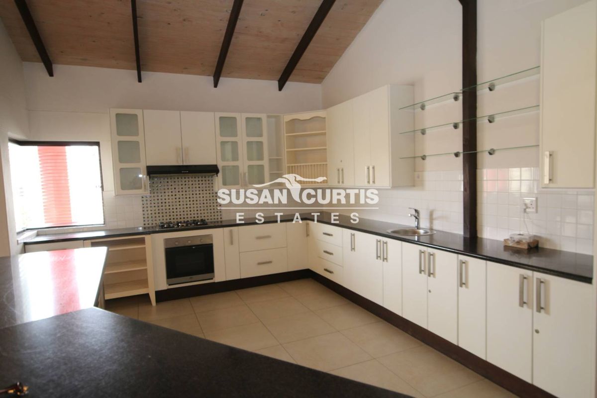 Spacious kitchen featuring white cabinetry, dark countertops, gas hob, built-in oven, and exposed timber beams under a vaulted ceiling.