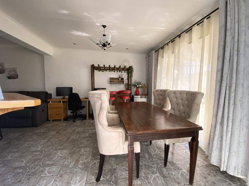 Open plan living and dining area featuring tiled flooring and large windows with curtain treatments, offering a versatile space for family living.