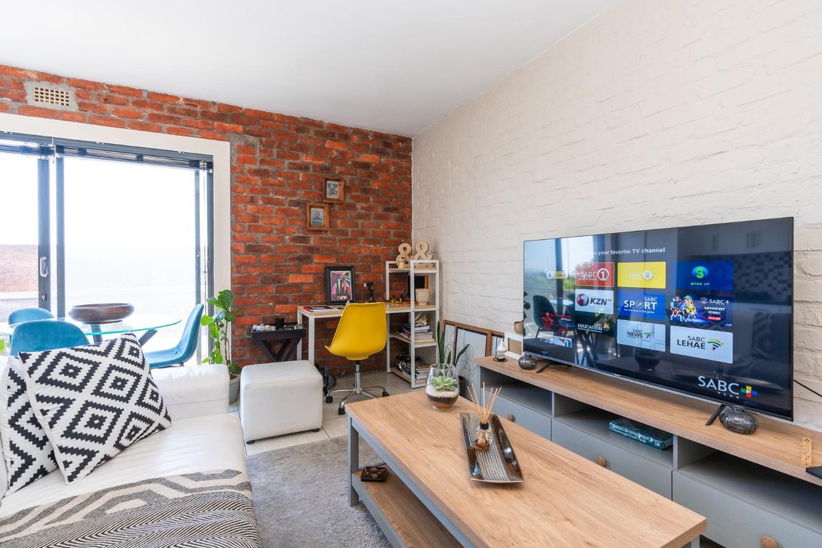 A cozy living room featuring a striking exposed brick wall, painted brick accent wall, and large sliding glass doors providing natural light.