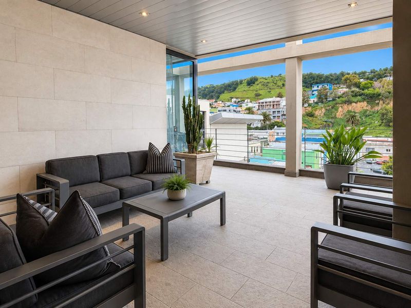 A spacious covered balcony featuring modern stone wall cladding, tiled flooring, and recessed lighting, offering an elevated view of the surrounding hillside.
