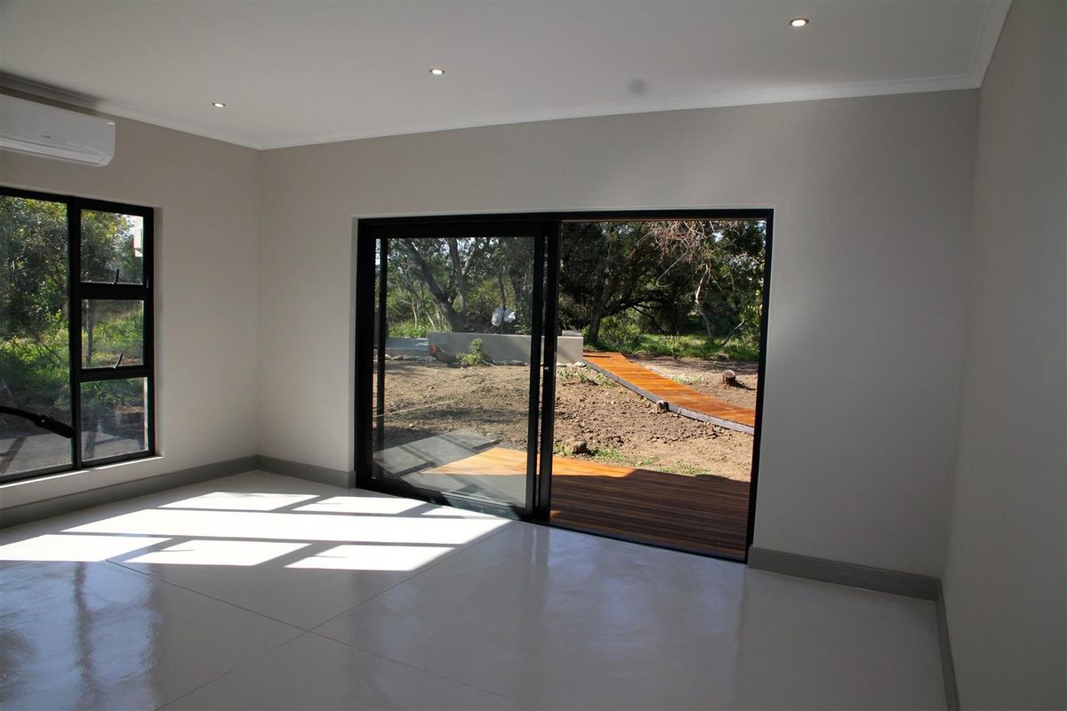 Bright living area featuring polished concrete floors, recessed lighting, split-system air conditioning, and large sliding glass doors opening to a wooden deck.