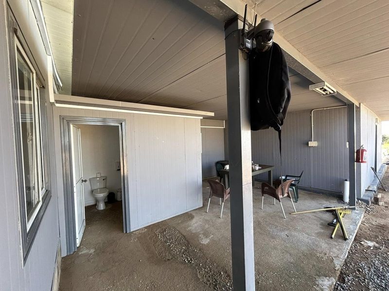 A covered outdoor patio area featuring concrete flooring, an integrated external toilet, and basic utility fixtures, suitable for renovation or functional outdoor use.