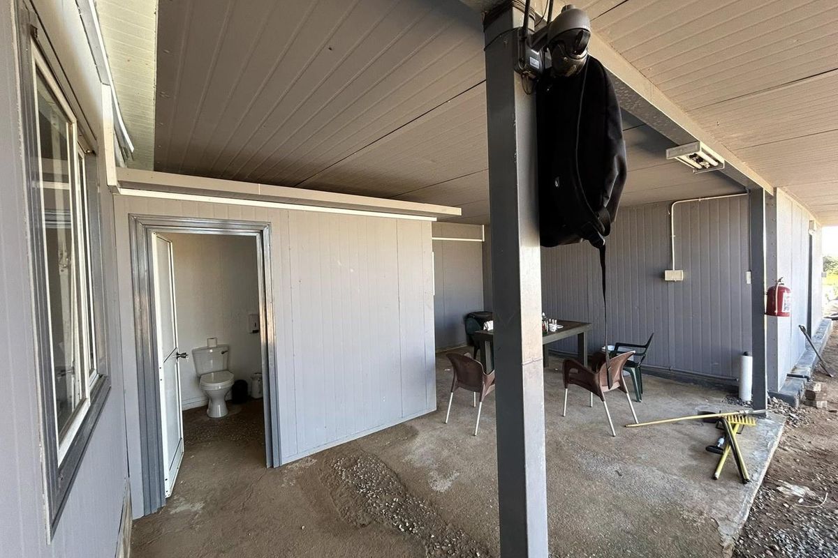 A covered outdoor patio area featuring concrete flooring, an integrated external toilet, and basic utility fixtures, suitable for renovation or functional outdoor use.