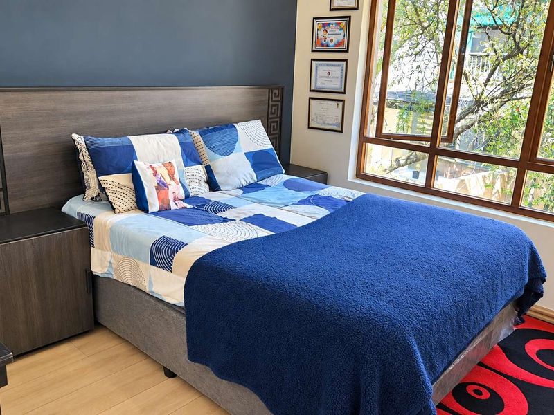 A well-maintained bedroom featuring a built-in headboard with integrated bedside tables and a large window providing natural light and garden views.