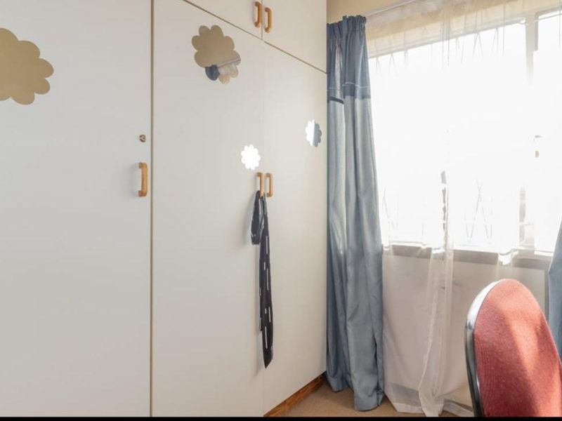 A bedroom featuring built-in cupboards and a large window allowing for natural light.
