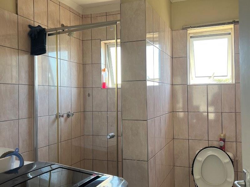 A functional bathroom featuring a shower enclosure, toilet, and neutral wall tiling. The space includes natural light from two windows.