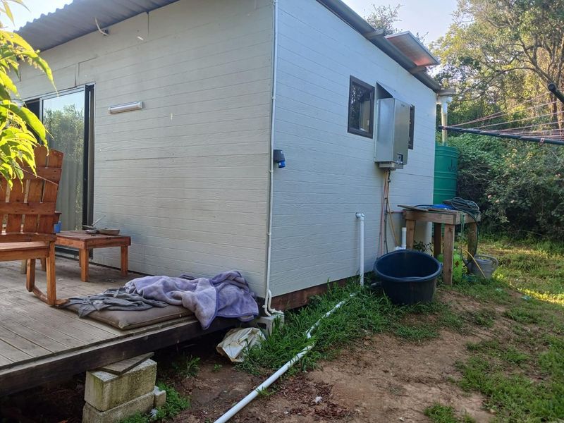 Rear view of the residential structure featuring timber decking, an external gas geyser, and a water storage tank set within a natural garden area.