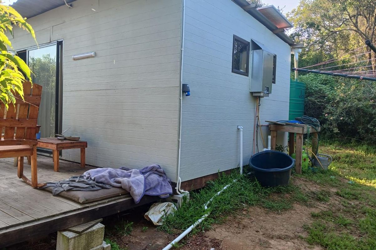 Rear view of the residential structure featuring timber decking, an external gas geyser, and a water storage tank set within a natural garden area.