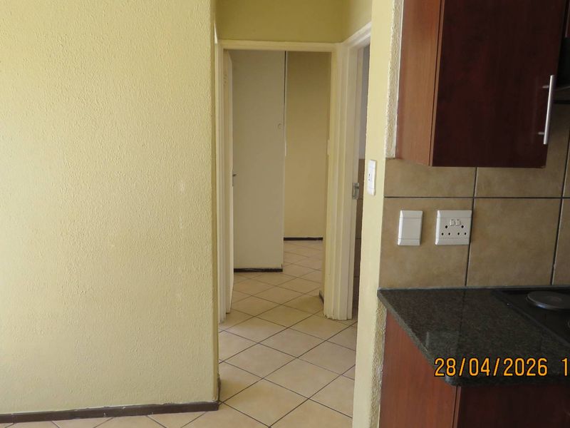 A functional kitchen area featuring built-in cabinetry, granite countertops, and an electric hob, leading into a hallway with tiled flooring.