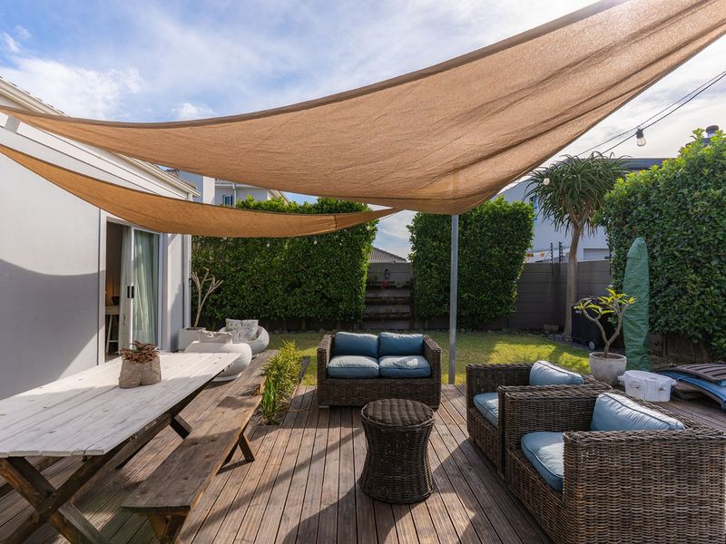 A well-maintained outdoor patio area featuring timber decking, a protective shade sail, and established garden hedging, providing a comfortable space for outdoor living.