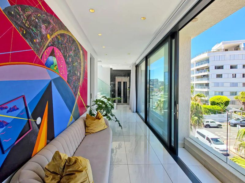 A modern, enclosed balcony featuring large sliding glass doors, polished tile flooring, recessed lighting, and a private elevator access with views of the surrounding area.