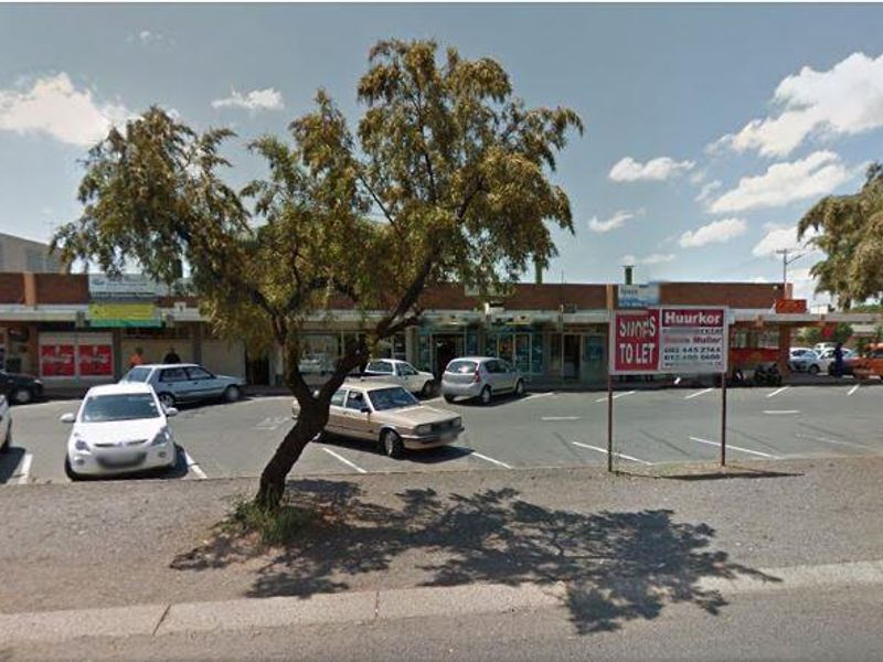Street-level view of a commercial retail strip center with an asphalt parking lot and storefront access.