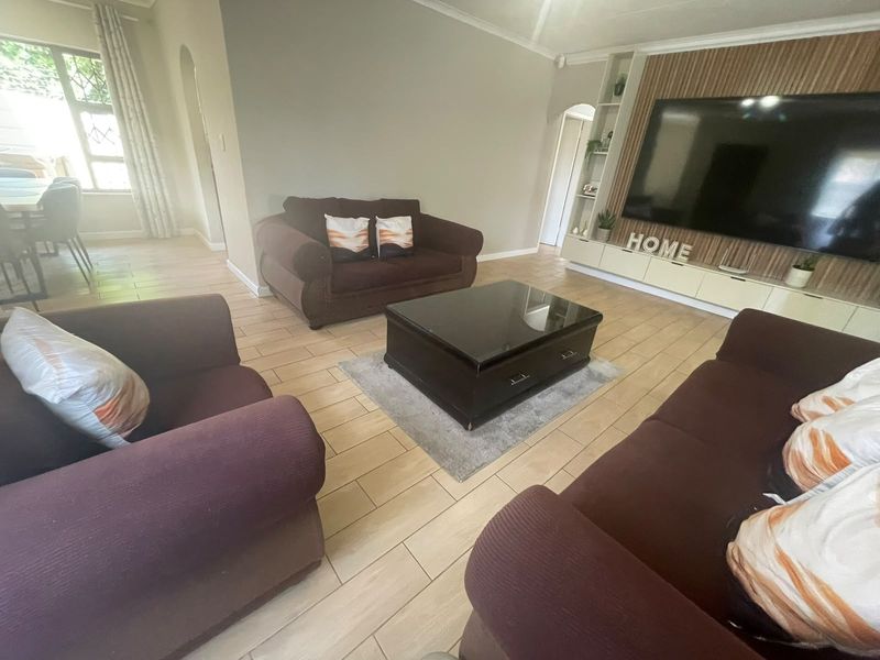 A comfortable living room featuring tiled flooring, a built-in media wall unit, and an archway leading to the adjacent dining area.