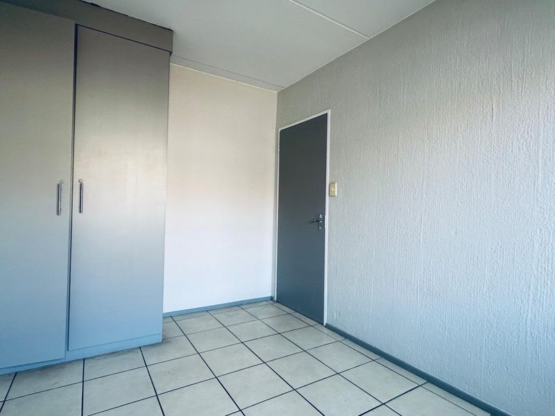 A clean, empty bedroom featuring neutral tiled flooring, a built-in wardrobe, and a simple internal door, offering a blank canvas for personalization.