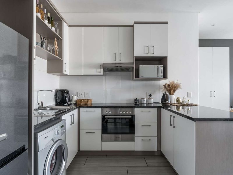 Modern kitchen featuring white cabinetry, granite countertops, integrated appliances including an oven, hob, extractor fan, and washing machine, with a clean tiled backsplash.