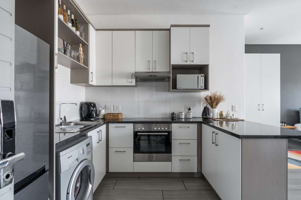 Modern kitchen featuring white cabinetry, granite countertops, integrated appliances including an oven, hob, extractor fan, and washing machine, with a clean tiled backsplash.
