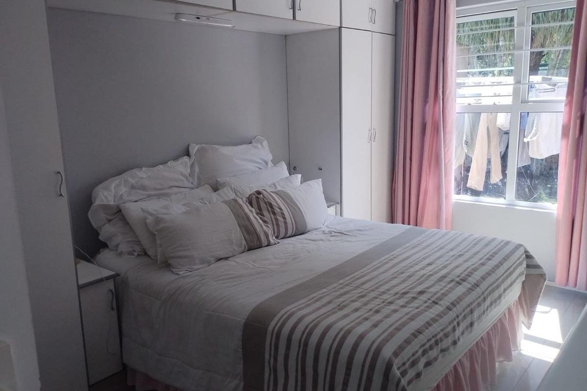 A bedroom featuring built-in cupboards with overhead storage, tiled flooring, and a window providing natural light.