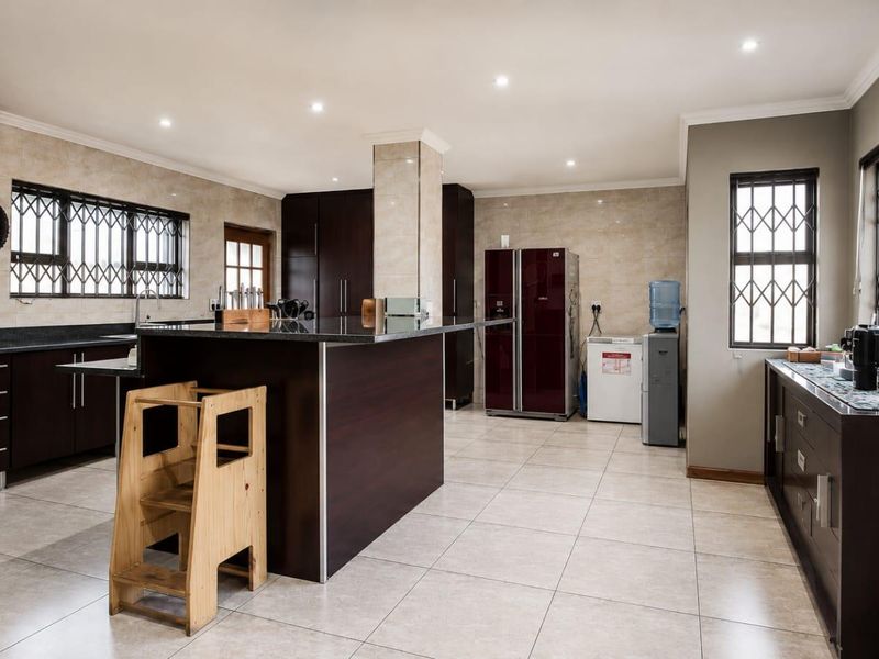 Spacious kitchen featuring dark wood cabinetry, granite countertops, a central island, and tiled flooring with recessed lighting throughout.