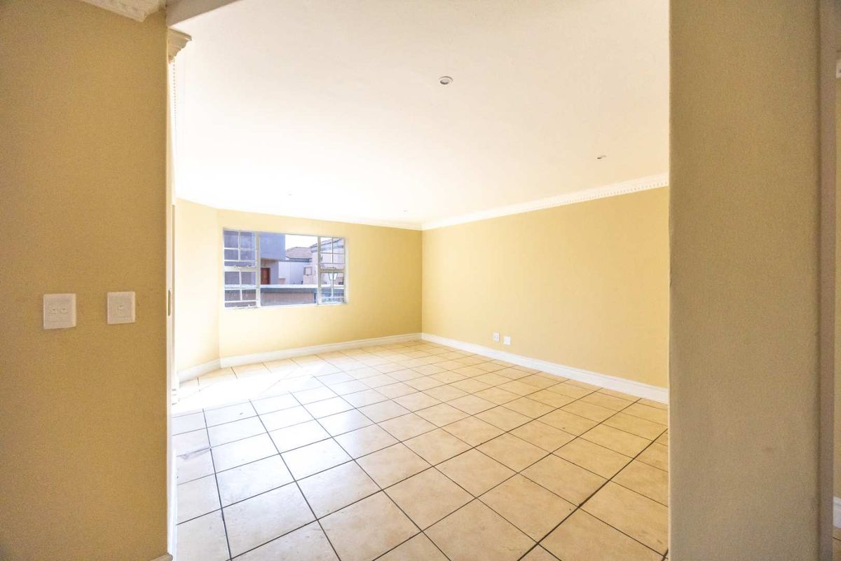 A bright, empty living area featuring neutral tiled flooring, recessed lighting, and classic cornice detailing, offering a versatile space ready for personalization.