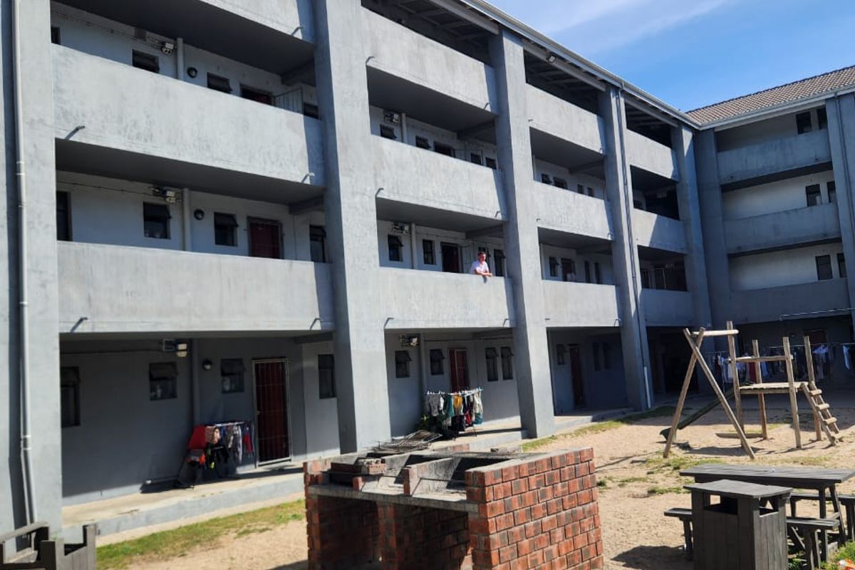 Exterior view of a multi-story residential apartment block featuring communal outdoor space with a brick braai and playground area.