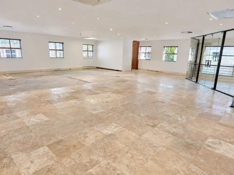 Spacious open-plan office area featuring travertine tile flooring, recessed lighting, and a modern glass partition overlooking the staircase.