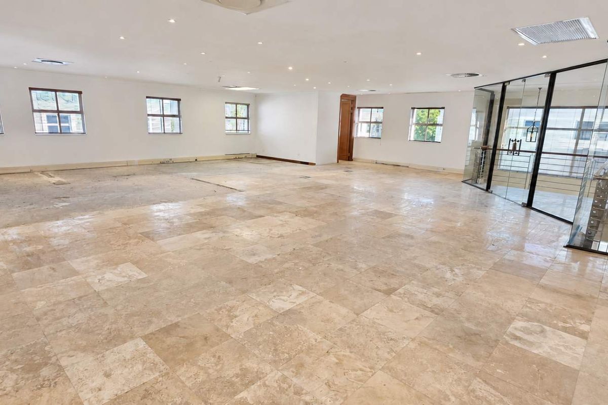 Spacious open-plan office area featuring travertine tile flooring, recessed lighting, and a modern glass partition overlooking the staircase.