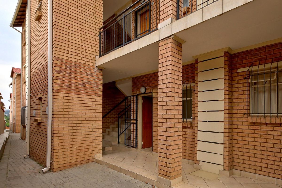 Exterior view of an apartment building featuring face brick construction, a covered patio area, and secure metal railings and window bars.