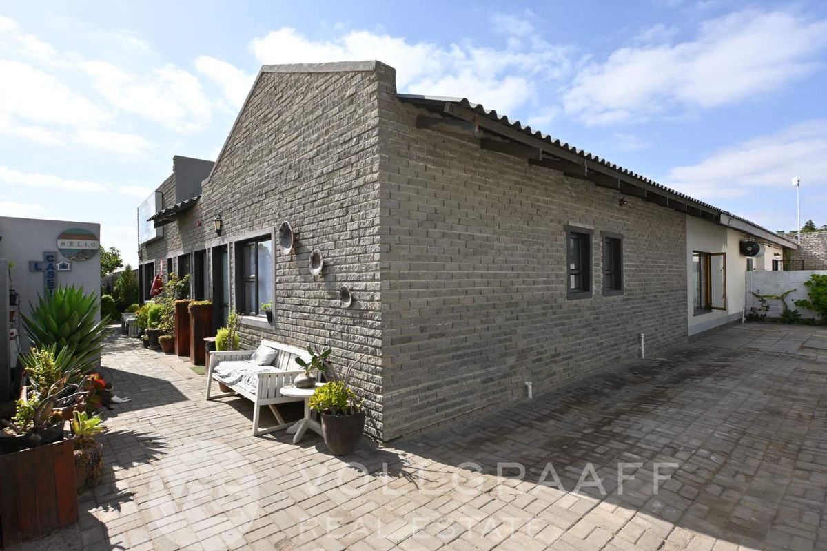 Exterior view of the guest house featuring textured brick facade, paved courtyard area, and corrugated roof structure.