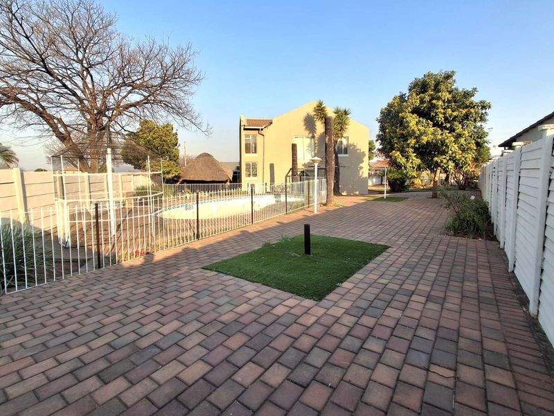 Spacious rear garden area featuring a paved patio, swimming pool with safety fencing, and a traditional thatched lapa structure.