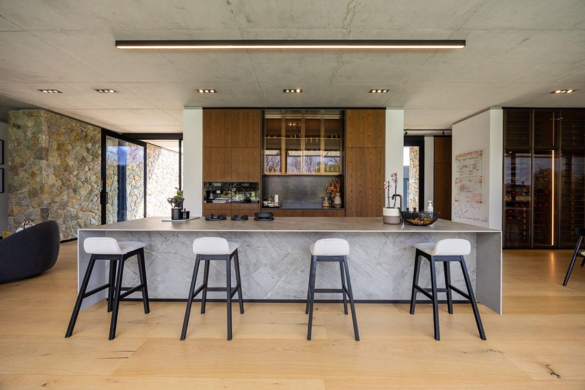 Modern open-plan kitchen featuring a large stone island, high-end cabinetry, integrated wine storage, and a striking exposed concrete ceiling with premium finishes.