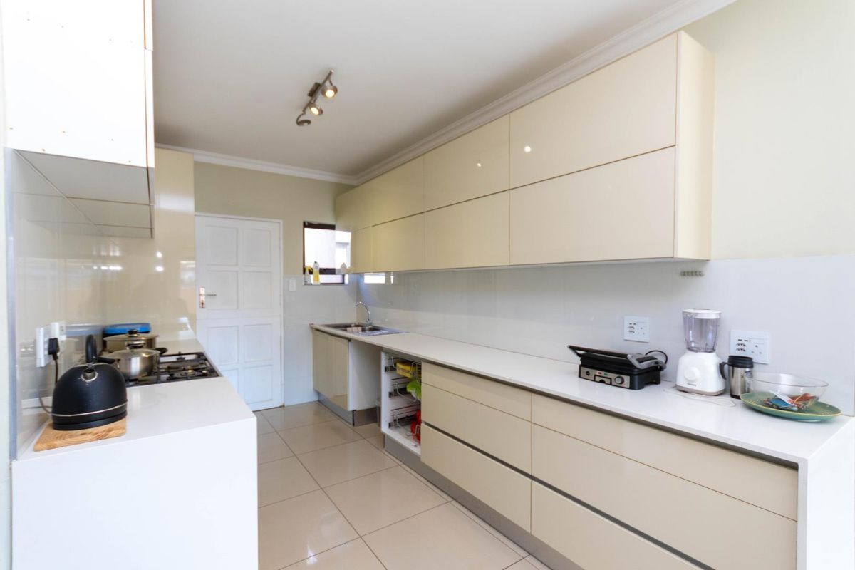 A modern galley-style kitchen featuring sleek cream cabinetry, white countertops, tiled flooring, and a built-in gas hob with an integrated sink area.