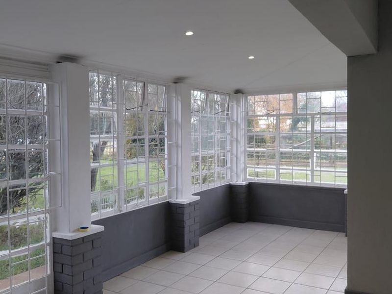 A bright, enclosed patio area featuring tiled flooring, recessed downlights, and extensive steel-framed windows overlooking the garden.
