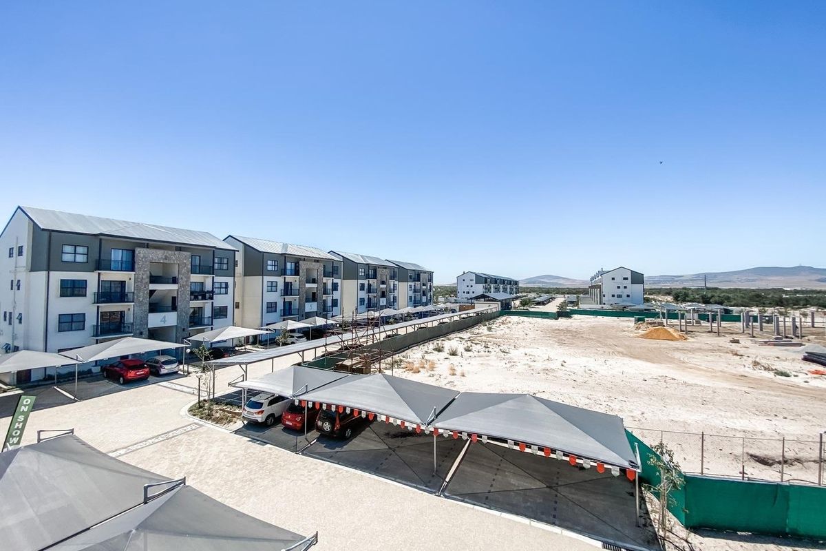 An elevated view of a modern apartment complex featuring paved parking areas with shade-cloth carports and surrounding undeveloped land.