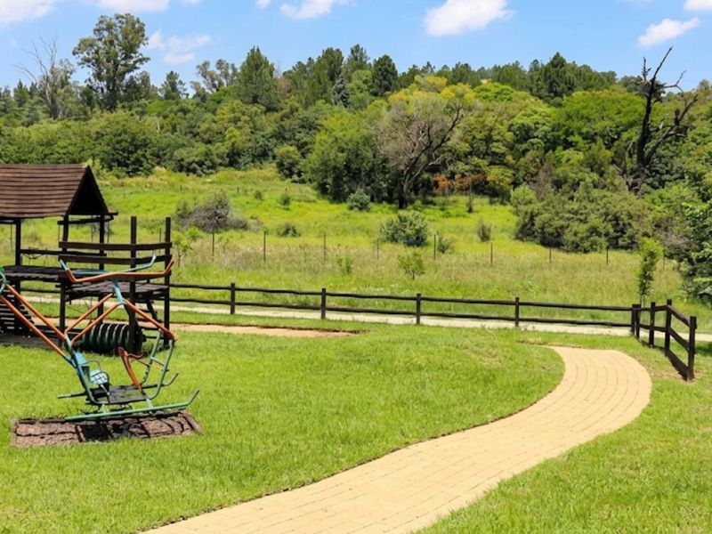 A well-maintained garden area featuring a paved walkway, timber fencing, and a playground structure set against a natural green landscape.