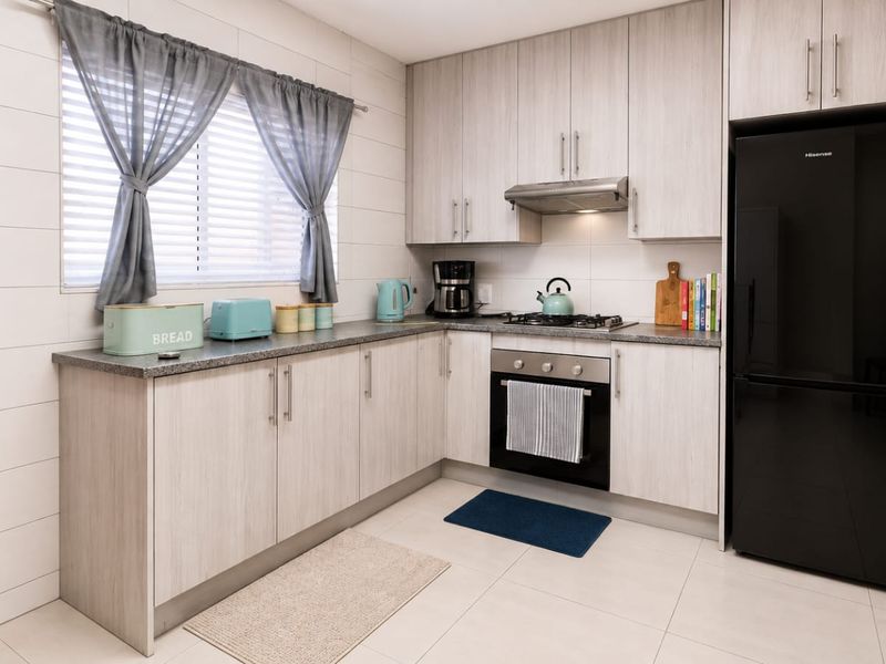 Modern kitchen featuring light wood-grain cabinetry, stone-look laminate countertops, built-in oven, gas hob, and stainless steel extractor fan.