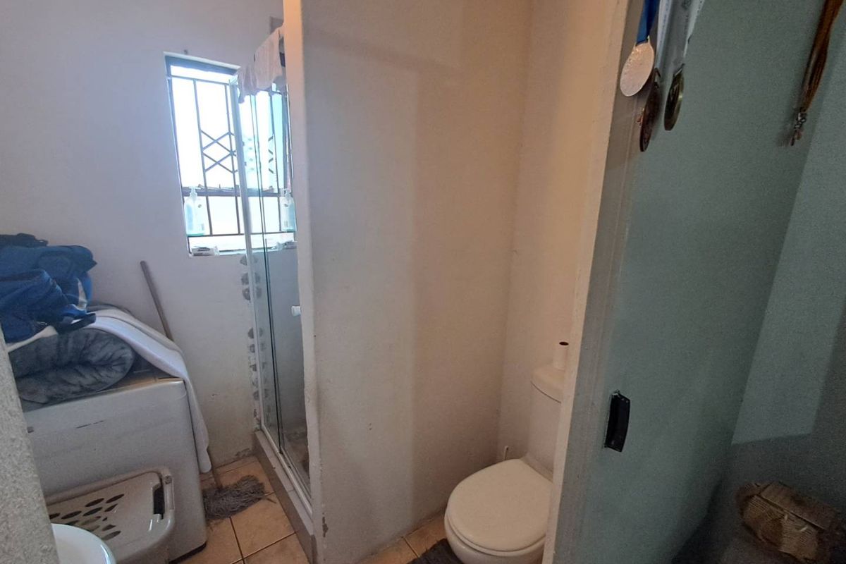 A functional bathroom featuring a shower enclosure, toilet, and tiled flooring, with a window providing natural light.
