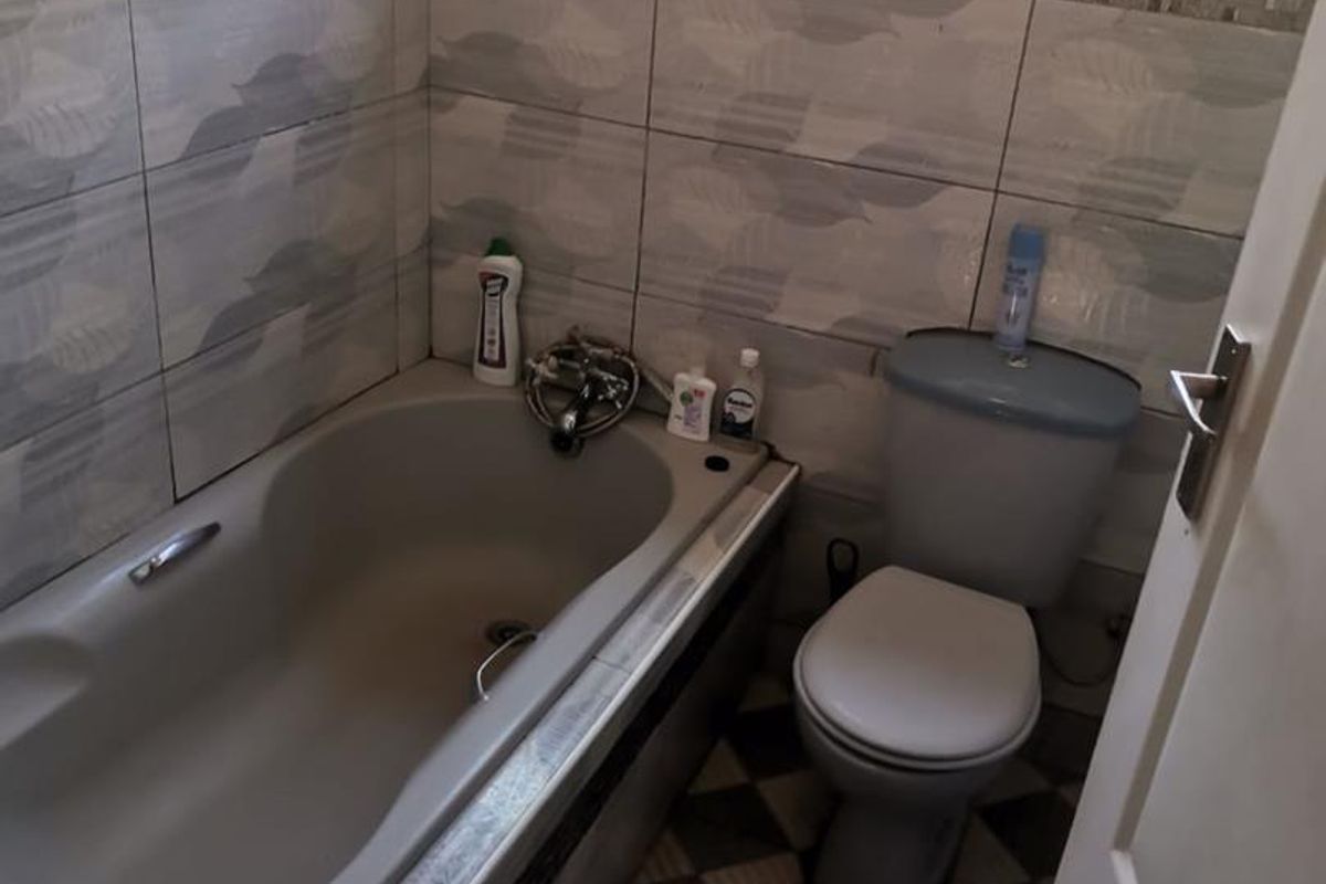 A compact bathroom featuring a built-in bathtub, a standard toilet, and tiled walls with a decorative mosaic border.