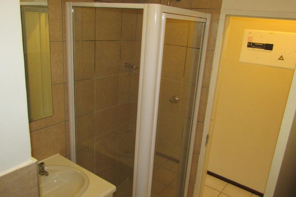 A functional bathroom featuring a shower enclosure, vanity basin, and tiled walls, with an integrated electrical distribution board located near the entrance.