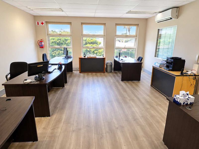 A spacious, well-lit office area featuring laminate flooring, a suspended ceiling with recessed lighting, and a wall-mounted air conditioning unit.
