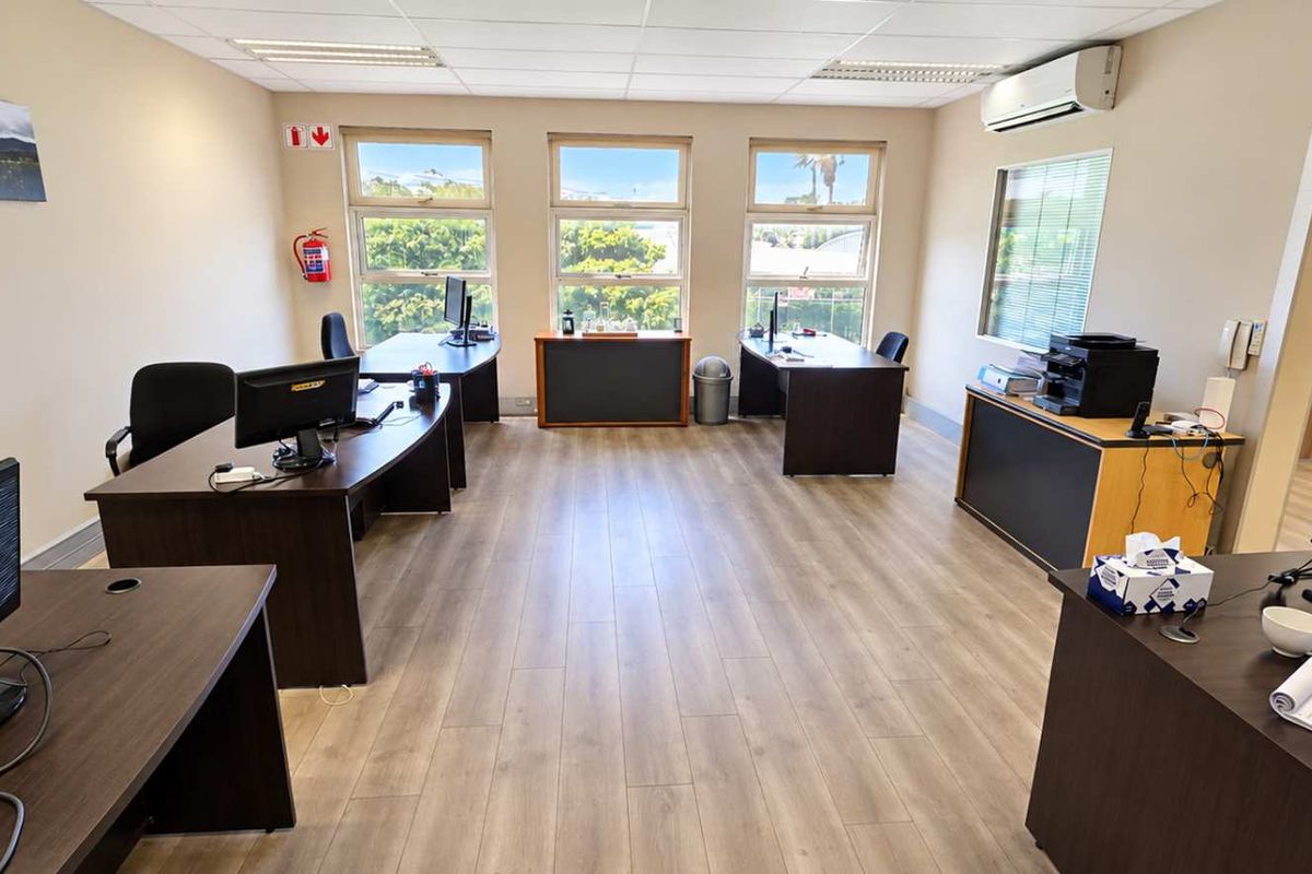 A spacious, well-lit office area featuring laminate flooring, a suspended ceiling with recessed lighting, and a wall-mounted air conditioning unit.