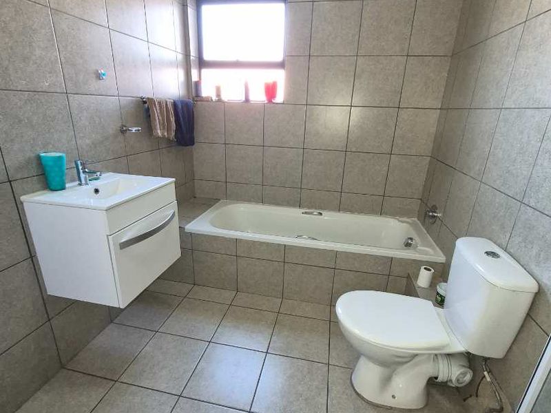 A functional bathroom featuring a wall-mounted vanity, built-in bathtub, and tiled finishes throughout.