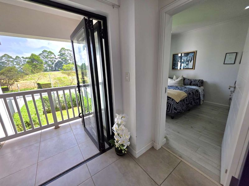A covered balcony featuring modern bi-fold glass doors, tiled flooring, and a railing, providing a seamless transition to the adjacent bedroom.