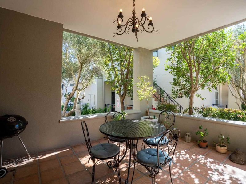A covered patio area featuring terracotta floor tiles, a decorative wrought iron chandelier, and a concrete balustrade overlooking a landscaped garden.